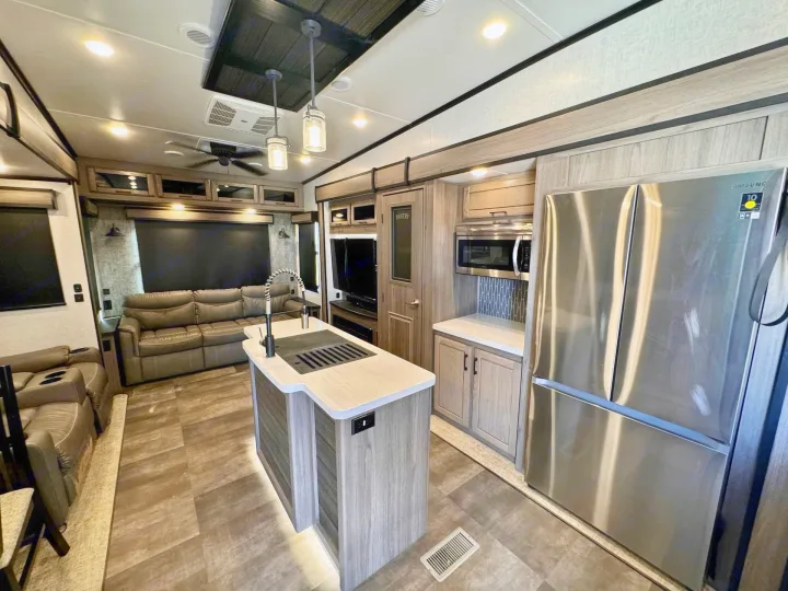 Spacious RV rental interior features a modern kitchen island with sink, stainless steel fridge, microwave, and comfy living area.. Crossroads RV Cameo 2021