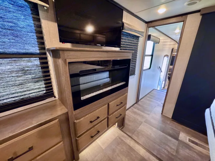RV rental interior: modern living space with TV, electric fireplace, storage drawers, window blinds, and a hallway view.. Crossroads RV Cameo 2021