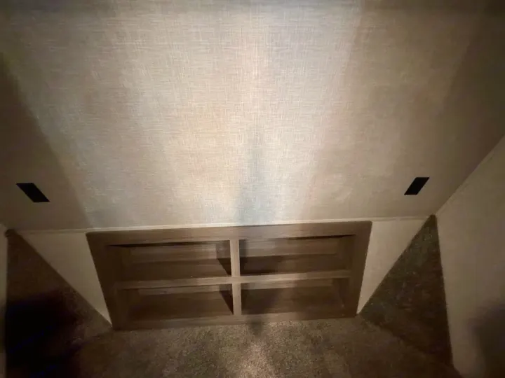 This RV rental interior features a cozy bunk area with built-in wooden shelving, angled carpeted walls, and light textured ceiling.. Crossroads RV Cameo 2021