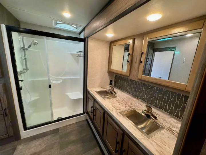 Well-appointed RV rental bathroom features a modern shower, double vanity with sleek sinks, and stylish tiled backsplash.. Crossroads RV Cameo 2021