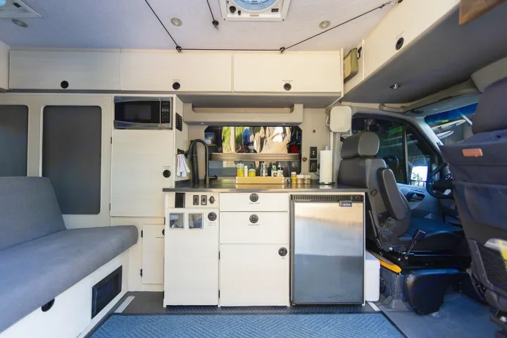 RV rental interior: organized kitchen with microwave, fridge, sink, ample cabinets, and a side lounge bed.. Sportsmobile 2500 2017