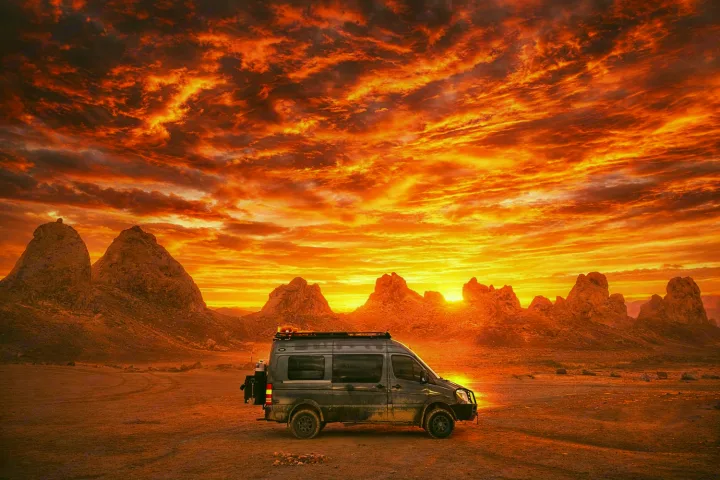 RV rental van parked in a dramatic desert landscape at sunset, with fiery orange and red skies over rocky mountains.. Sportsmobile 2500 2017