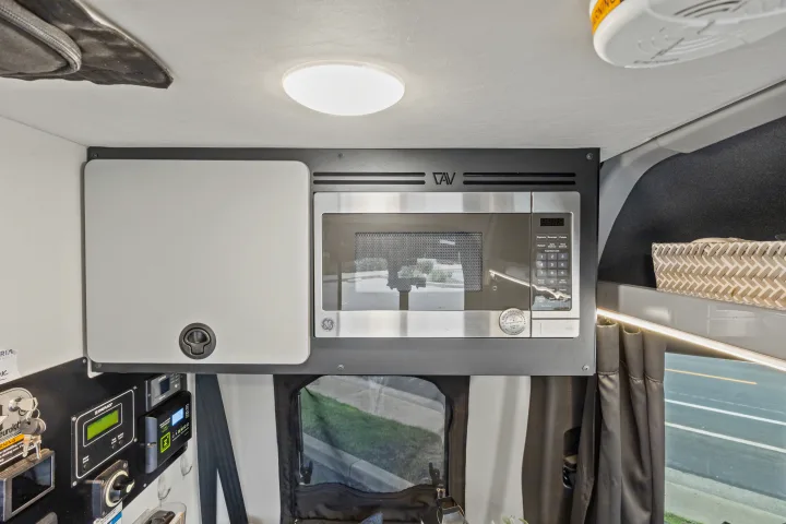 Modern rv rental interior features a GE microwave, control panel, storage cabinet, and ambient lighting.. Winnebago Revel 2023