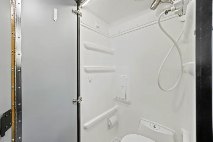 Inside a compact white wet bath for an RV rental, featuring a shower, toilet, and shelves, designed for travel.. Winnebago Revel 2023