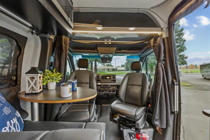 RV rental's inviting interior: dinette with table, cozy front seats, overhead storage, and kitchen amenities for comfortable travel.. Winnebago Revel 2023