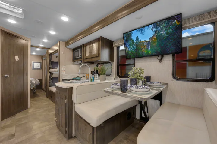 Spacious RV rental interior: a modern kitchen, dining area with a set table, cozy bunk beds, and a large wall-mounted TV.. Coachmen Pursuit 2022