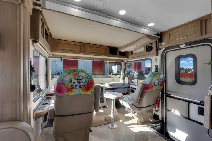 Inside an RV rental: the front cockpit with colorful 'Skipper Seat' covers, a raised overhead bed, dashboard, and entry door.. Forest River Georgetown 2019