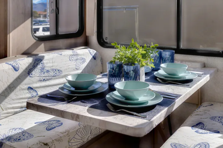 Cozy rv rental dining area with light blue place settings, blue glasses, and butterfly-patterned cushions. Sunlit interior details.. Forest River Georgetown 2019