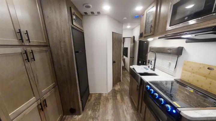 RV rental kitchen and hallway: Modern interior featuring a stove, microwave, sink, fridge, and ample cabinets.. Forest River Cherokee Wolf Pack 2021