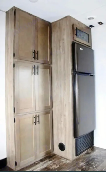 RV rental kitchen: light wood cabinets with black handles, a built-in black refrigerator, and various storage.. Forest River Cherokee Wolf Pack 2021