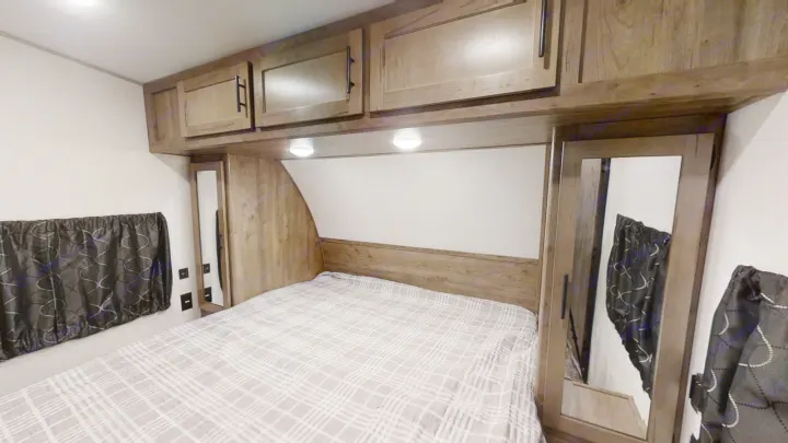 Explore this compact RV rental bedroom with a comfy bed, storage cabinets, and mirrored wardrobe doors.. Forest River Cherokee Wolf Pack 2021