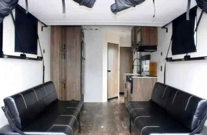 Spacious modern RV rental interior featuring kitchen, twin black sofas, and convertible sleeping areas for comfort.. Forest River Cherokee Wolf Pack 2021