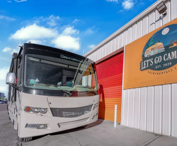 A Georgetown RV, available for rv rental, parked by a building with a "Let's Go Camping" banner and red roll-up door.. Forest River Georgetown 2019