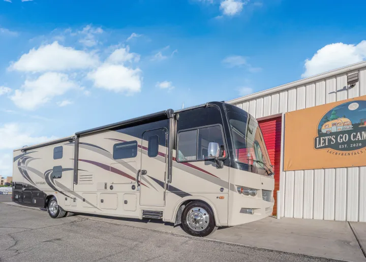 A beige & black Georgetown motorhome, an ideal RV rental, parked by a "Let's Go Camping" sign under a blue sky. Travel-ready.. Forest River Georgetown 2019