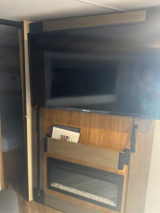 Inside an RV rental: a TV, built-in electric fireplace with decorative crystals, and adjacent bunk beds provide comfort on the go.. Forest River Campsite Reserve 26CJ 2025