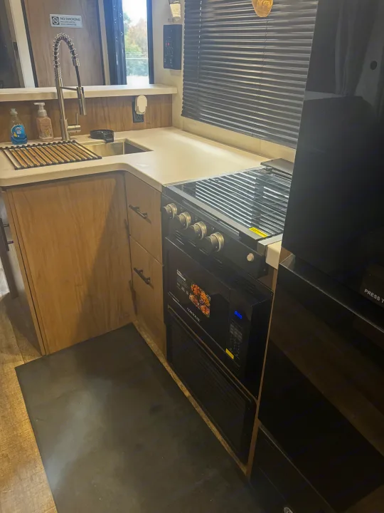 This RV rental kitchen features a modern sink, stovetop, oven, and microwave integrated into light wood cabinetry.. Forest River Campsite Reserve 26CJ 2025