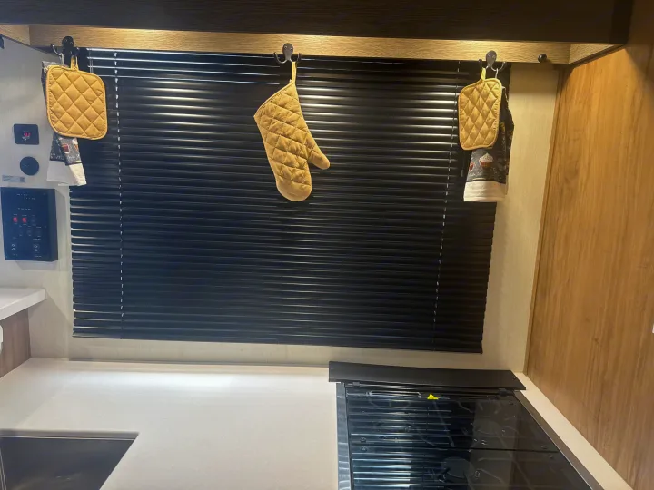 Compact rv rental kitchen featuring a cooktop, counter, black blinds, and neatly hung potholders & mitts. Ready for use!. Forest River Campsite Reserve 26CJ 2025