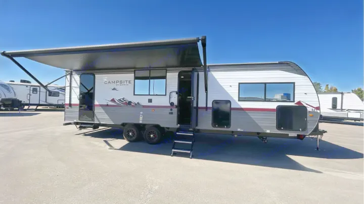Ready for your next adventure, this gray and white travel trailer RV rental features an extended awning, open door, and steps. Parked outdoors.. Forest River Campsite Reserve 26CJ 2025