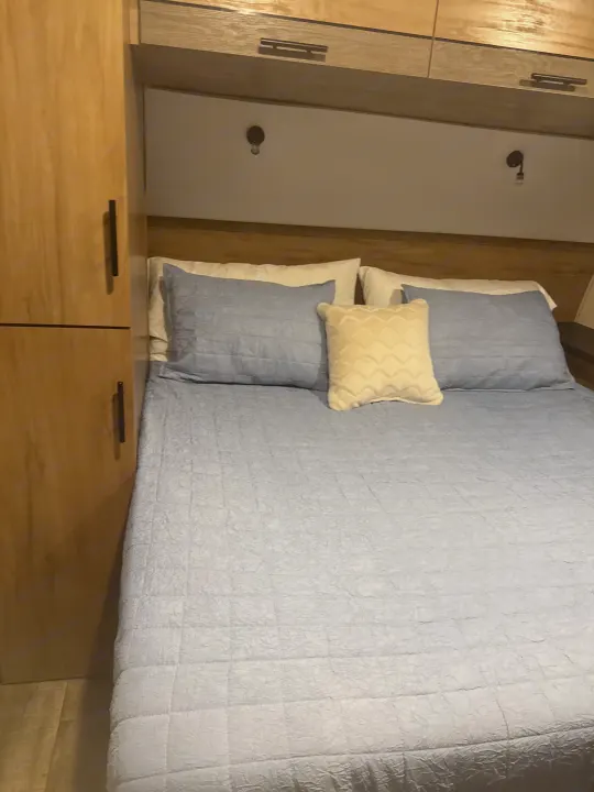 Comfortable RV rental bedroom with light blue quilted bedding, cream and white pillows, and light wood cabinetry.. Forest River Campsite Reserve 26CJ 2025