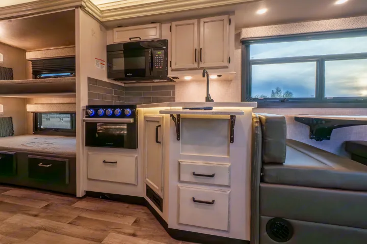 Inside a stylish rv rental: kitchen with microwave, oven, sink, plus comfortable bunk beds and dinette seating.. Entegra Coach Odyssey 2023