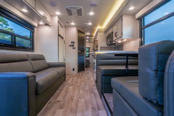 Modern RV rental interior with a comfortable gray sofa, dining area, and kitchen setup. Bright living space for travel.. Entegra Coach Odyssey 2023