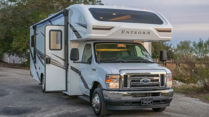 Bright white Entegra Class C rv rental on a Ford E-series chassis with door open, parked on an outdoor lot.. Entegra Coach Odyssey 2023