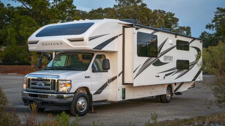 White Entegra Odyssey Class C motorhome, an ideal rv rental for outdoor adventures, parked with slide-out extended.. Entegra Coach Odyssey 2023