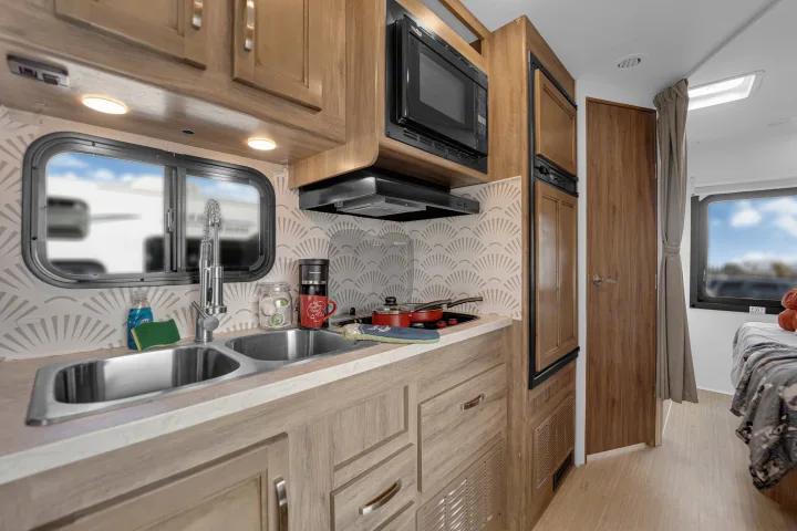 RV rental interior: modern kitchen with sink, microwave, stovetop, and coffee maker, leading to a cozy bedroom area.. Jayco Redhawk 2021
