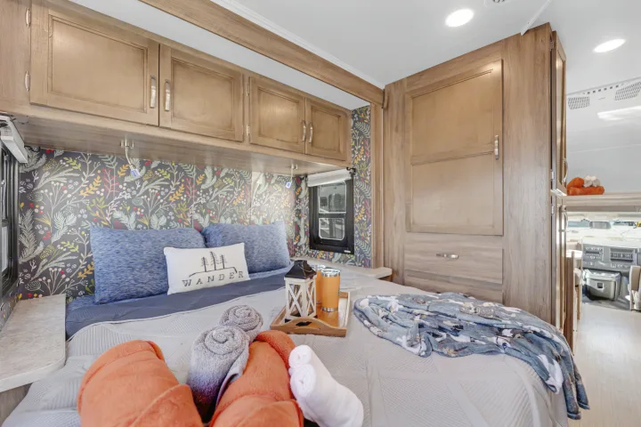 Experience comfort in this RV rental's cozy bedroom, featuring floral wallpaper, wooden cabinets, and a warm setup.. Jayco Redhawk 2021