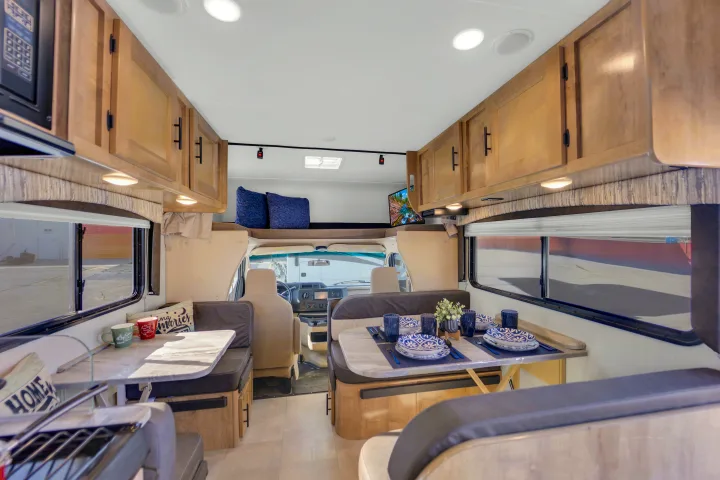 This rv rental interior features dual dinettes, overhead storage, and a cozy bed above the driver's cabin.. Coachmen Leprechaun 2021