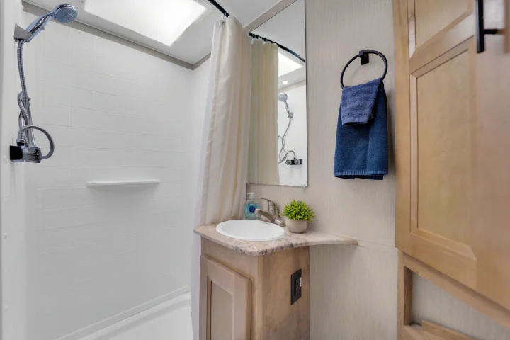 Compact RV rental bathroom with a bright white shower, light curtain, vanity, sink, mirror, and towel for comfortable trips.. Coachmen Leprechaun 2021