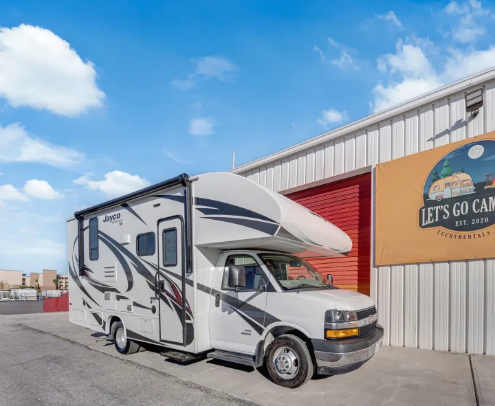 White Jayco Redhawk RV rental parked by a building under a blue sky, ready for camping and travel adventures.. Jayco Redhawk 2021