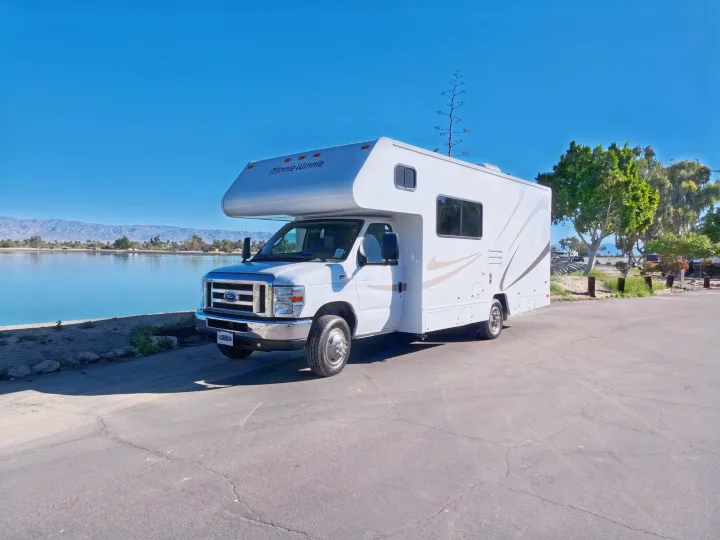 White Minnie Winnie rv rental (Class C) by a clear lake with mountains & blue sky. Perfect for scenic trips.. Winnebago Minnie Winnie 2020