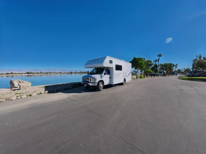 An RV rental (Minnie Winnie motorhome) parked by a serene lake, mountains, and clear blue sky, ideal for travel.. Winnebago Minnie Winnie 2020