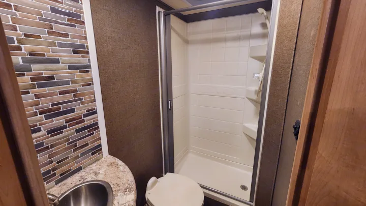 Compact RV rental bathroom with shower, toilet, and vanity featuring a stylish tile backsplash.. Thor Chateau 2019