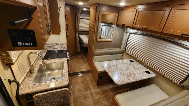 Spacious rv rental interior showcasing a kitchen with sink and stove, dinette seating with table, and a glimpse of the bedroom.. Thor Chateau 2019