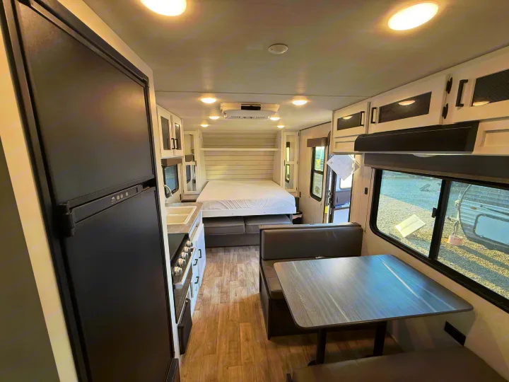 Bright rv rental interior: modern kitchen with fridge, sink, stove; dining booth; comfortable bed area. Ready for your adventure.. Keystone Hideout 2022