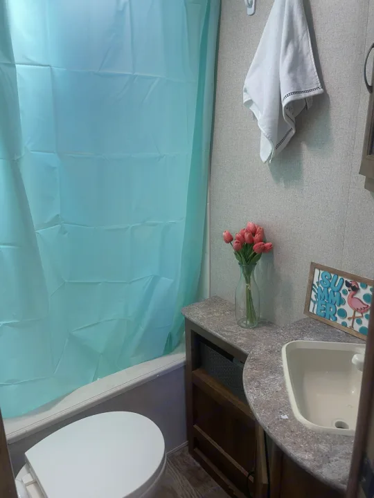 Cozy RV rental bathroom featuring a blue shower curtain, toilet, sink vanity with pink flowers & summer decor.. Crossroads RV Zinger 2017