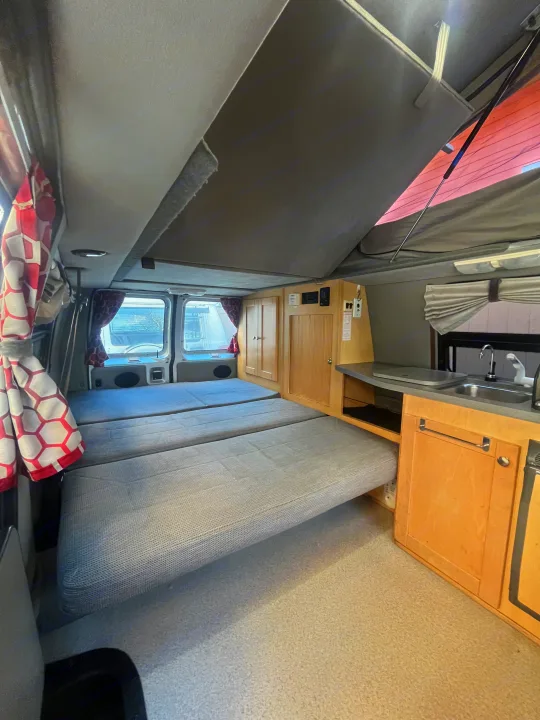 Inside an RV rental: cozy camper van interior with pop-top roof, fold-down beds, and a compact kitchenette.. Pleasure-Way Pleasure-Way Class B 2002