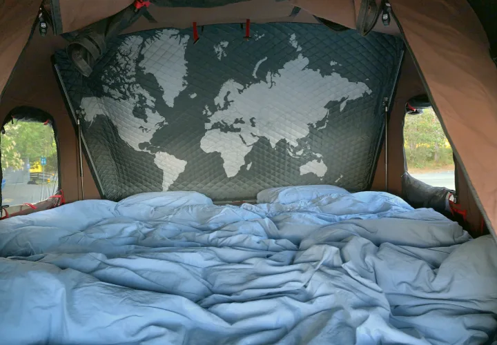 Cozy RV rental rooftop tent interior. Features a comfortable bed, quilted world map decor, and windows to nature for camping.. Toyota 4Runner 2017