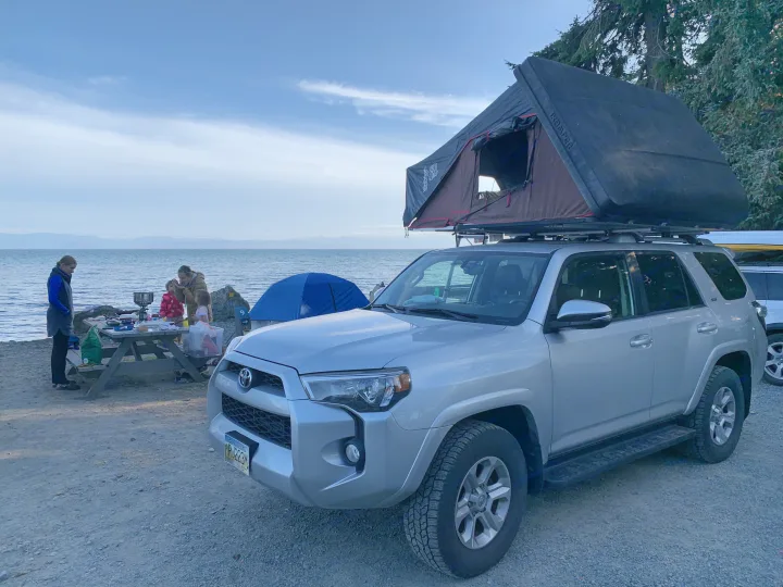 Family enjoying beach camping with a Toyota 4Runner and an RV rental roof-top tent, cooking by the water.. Toyota 4Runner 2017