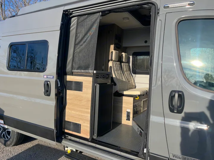 Modern rv rental camper van, side view with open door. See inside: kitchenette, passenger seats, and outside details.. Winnebago Solis 2025