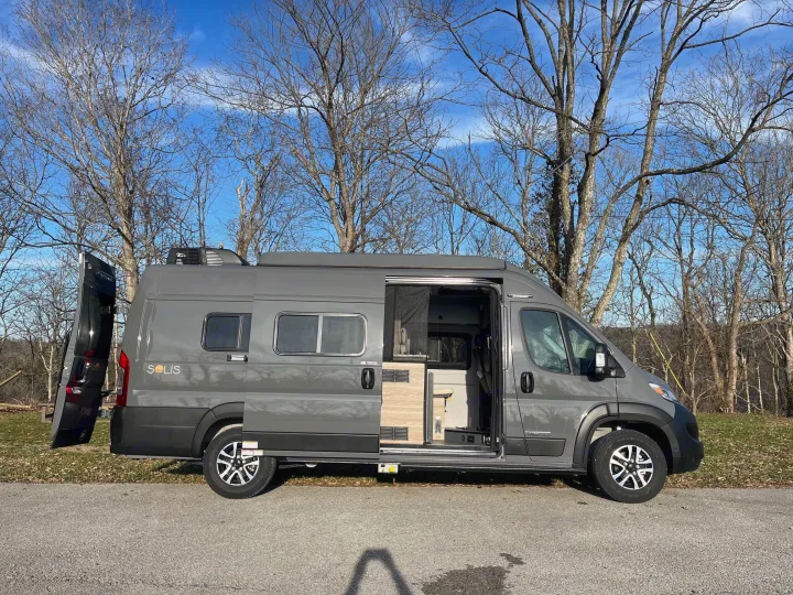 rv rental: A gray Winnebago Solis camper van with open doors, parked outdoors under bare trees on a sunny day.. Winnebago Solis 2025