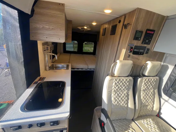 Explore this modern Winnebago rv rental interior: a full view of the kitchenette, rear bed, quilted passenger seats, and control panel wall.. Winnebago Solis 2025