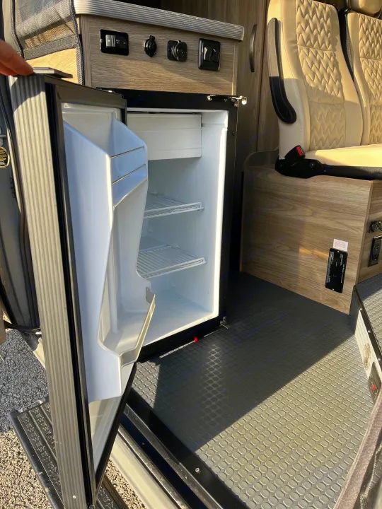 RV rental camper van interior. Features an open mini-fridge, kitchen controls, and stylish quilted seating for your travels.. Winnebago Solis 2025
