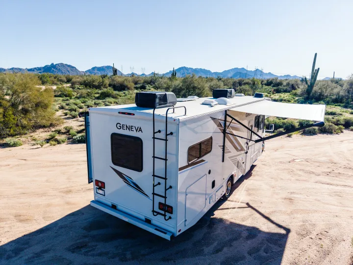 A white Geneva RV rental with an extended awning in a sunny desert landscape with mountains and saguaro cacti.. Thor Geneva 2025