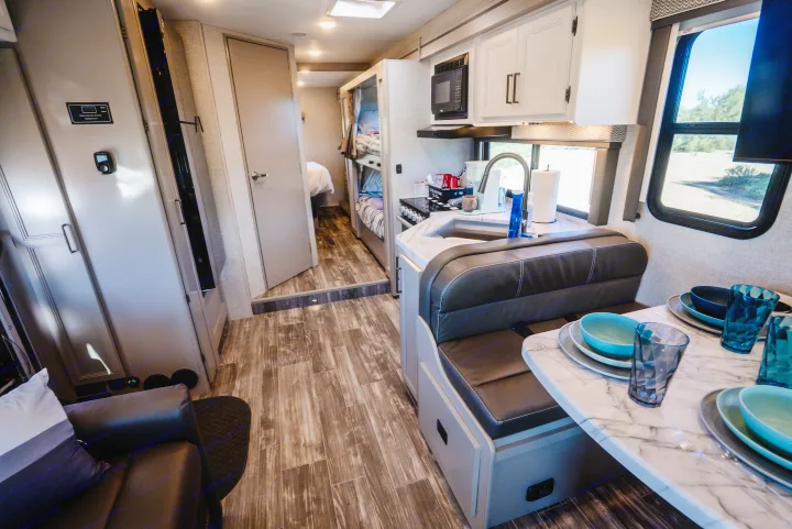 Spacious rv rental interior showing a full kitchen, dinette with dishes, and bunk beds. Perfect for a family adventure.. Thor Geneva 2025
