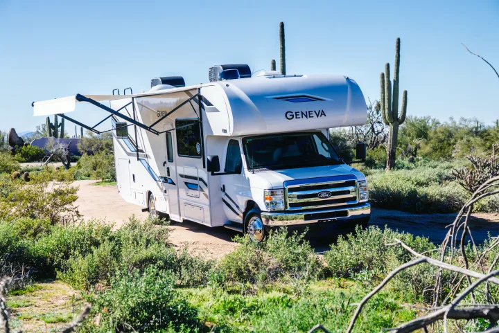 A white Geneva Ford Class C rv rental with an extended awning, parked in a sunny desert landscape among saguaro cacti.. Thor Geneva 2026