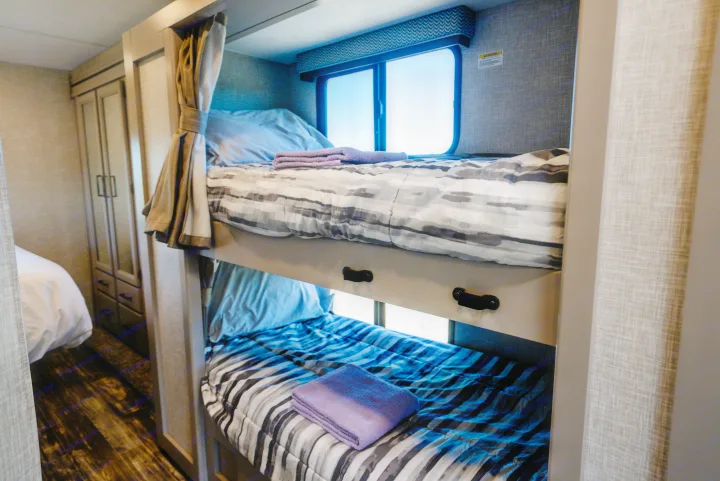 Cozy RV rental bunk beds, complete with fresh bedding and scenic windows, provide comfortable sleeping for road trip adventures.. Thor Geneva 2026