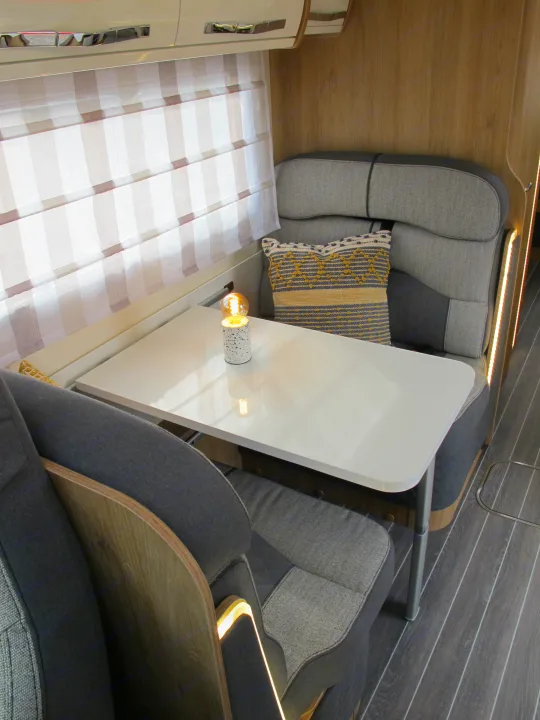 RV rental's cozy dining and seating area, featuring a white table, gray upholstered benches, and window blinds.. rollerteam 747 2021